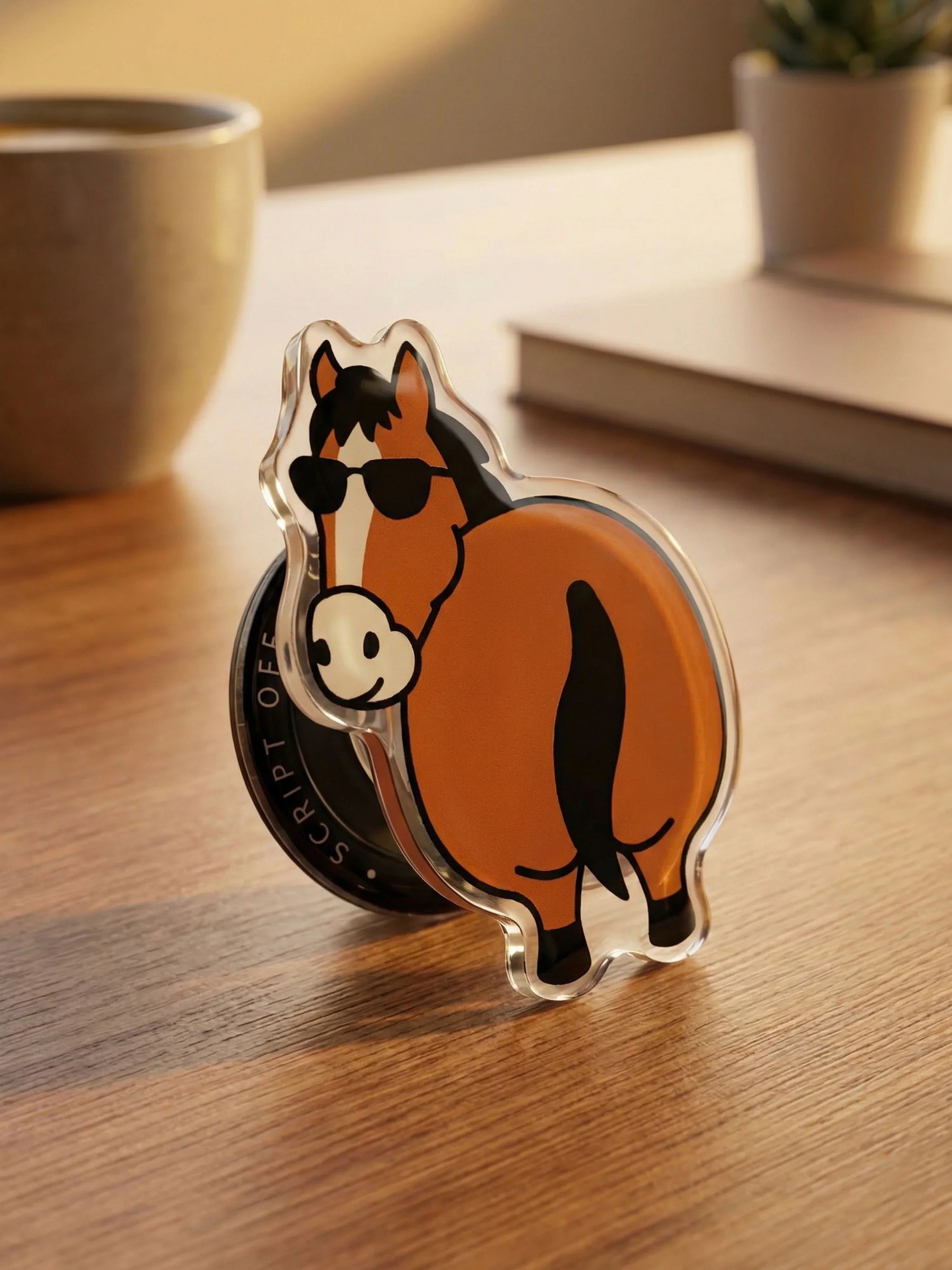 Brown Flattery Little Horse MagSafe grip wearing sunglasses, standing upright on wooden desk with coffee and plant