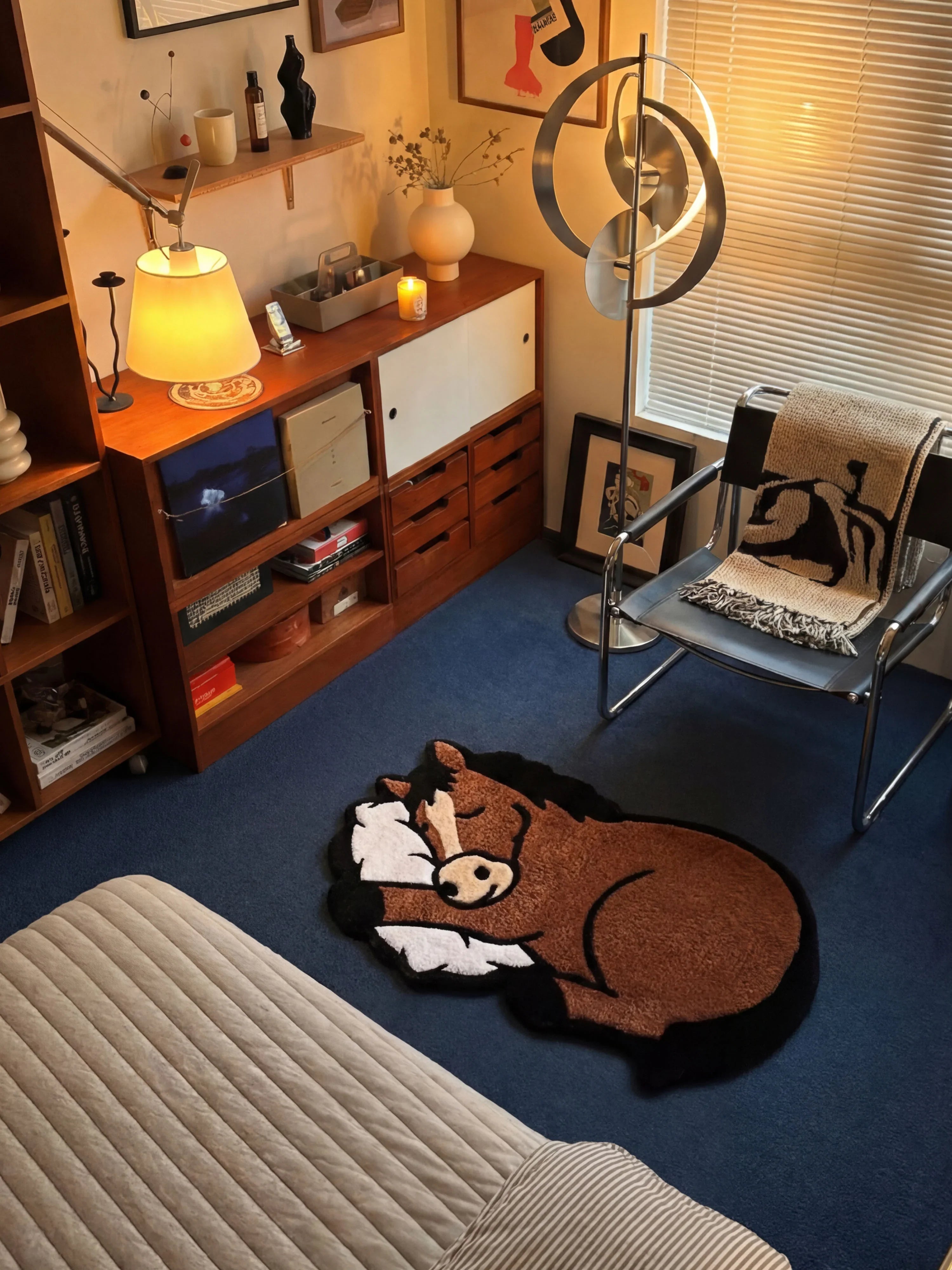 Sleep Right Neigh horse rug beside bed in mid-century modern bedroom with blue carpet, walnut shelving, and warm lamp lighting