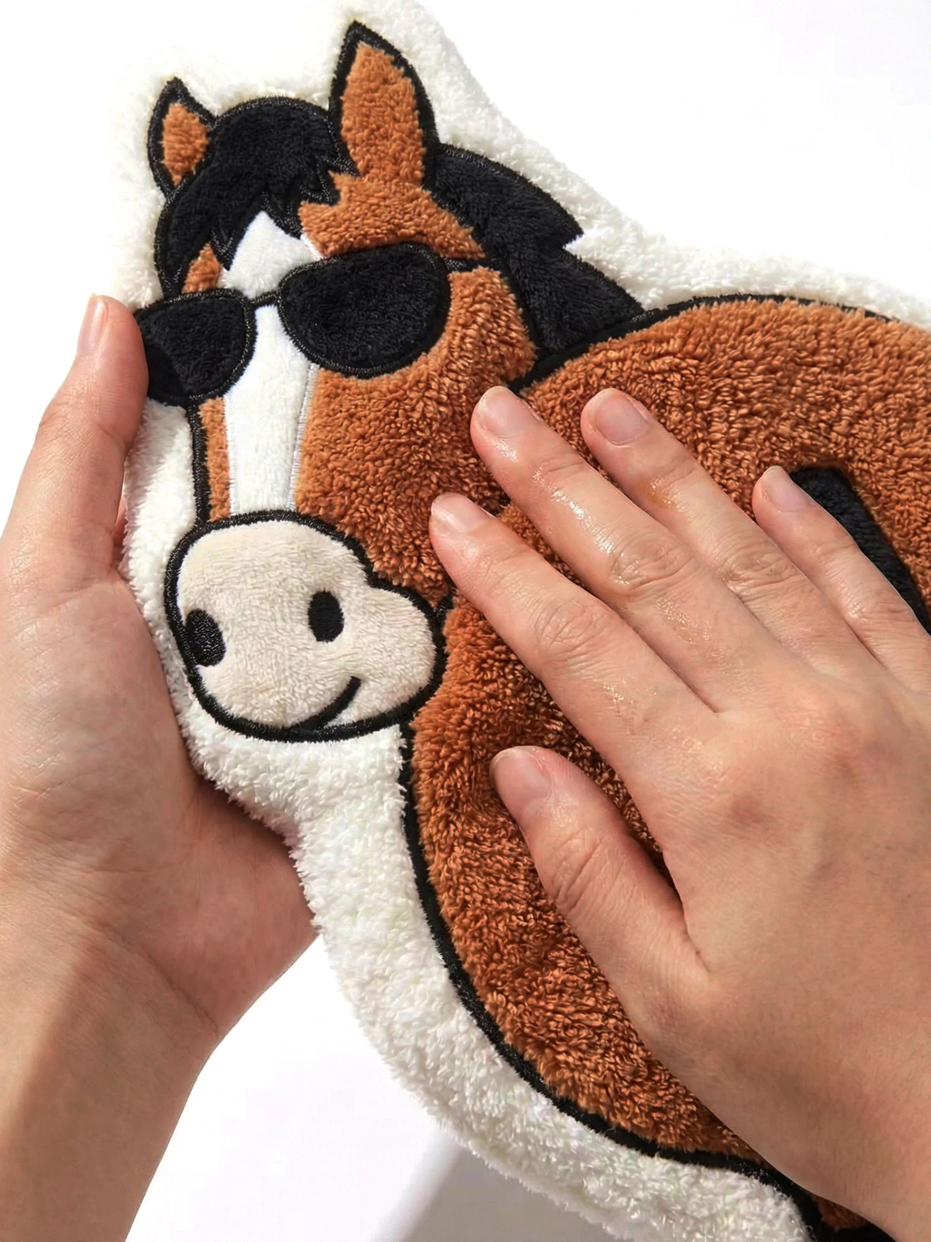 Close-up of hands holding soft embroidered Year of the Horse Flattery cartoon hand towel, highlighting texture and face detail